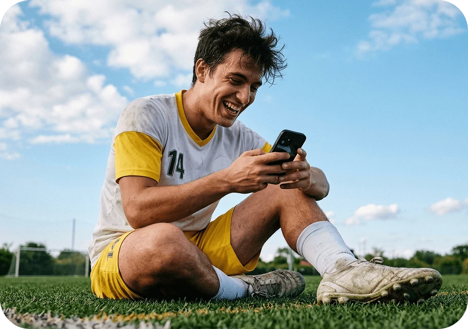Jogador de futebol sentado no gramado acessando o Copa10 no celular